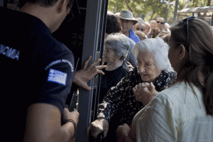 Un policía griego abre la puerta de un banco en Atenas para permitir que una anciana retire un máximo de 120 euros por semana Foto: AP