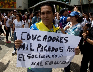 In this Thursday, May 28, 2015 photo, a teacher holds a poster that reads in Spanish " Teachers underpaid by rude socialism" during a protest in Venezuela's Central University, UCV, in Caracas, Venezuela. College professors in this socialist country plagued by a cash crunch, shortages and spiraling inflation are abandoning their jobs in droves, unable or unwilling to survive on salaries as minuscule as $30 per month. (AP Photo/Fernando Llano)