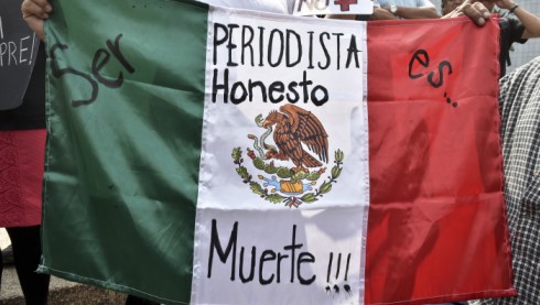 A woman holds Mexican flag with an inscription that reads "To Be a Honest Journalist is Death" during a demonstration for the murder of photojournalist Ruben Espinoza, at Angel of Independence square in Mexico City, on August 2, 2015. Espinosa was found shot dead on August 1, 2015, in Mexico City, where he had moved two months ago from Veracruz, after reporting strong threats from the government of the state. Since 2010, 11 journalists have been killed and four others have gone missing in Veracruz. AFP PHOTO/ Yuri CORTEZ (Photo credit should read YURI CORTEZ/AFP/Getty Images)