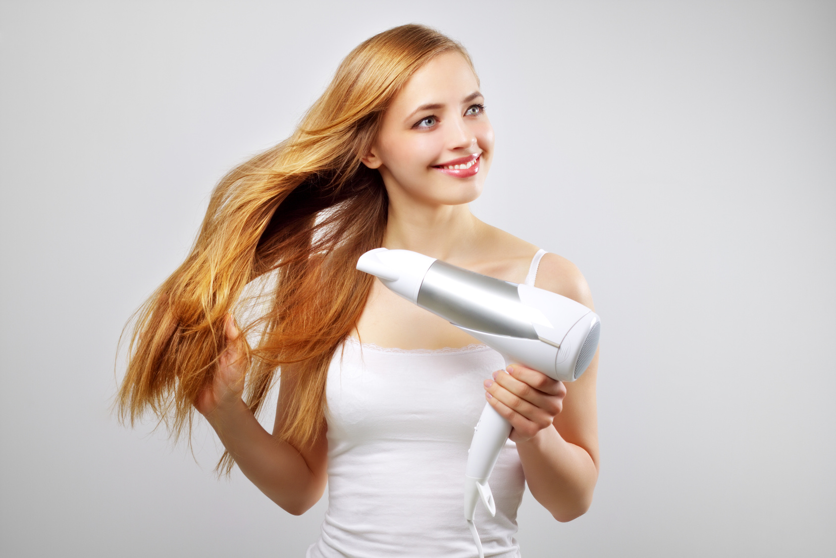 Beautiful smiling girl drying her hair with a blow dryer